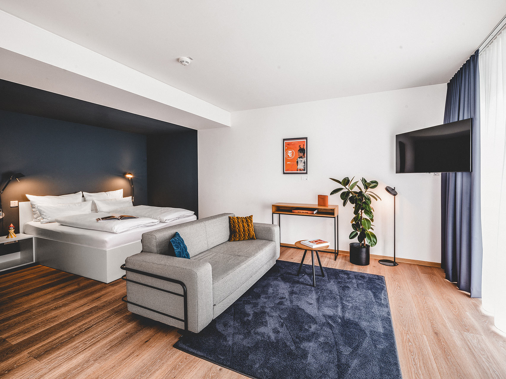 Modern eingerichtetes Apartment mit Doppelbett, grauem Sofa, blauem Teppich und Kunstdruck in einer Unterkunft in Herzogenaurach