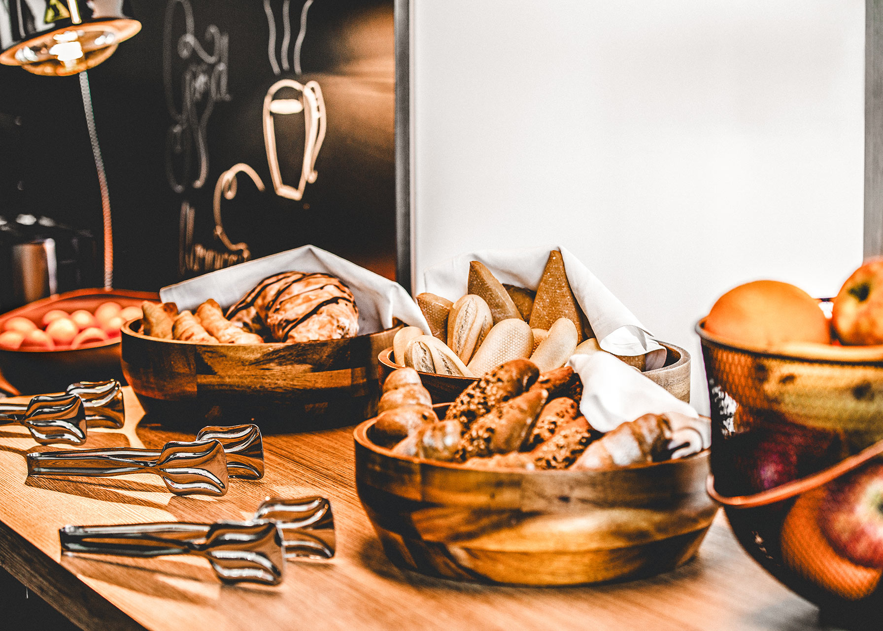 Frühstücksbuffet mit Brötchen, Croissants und frischem Obst in Holzschalen
