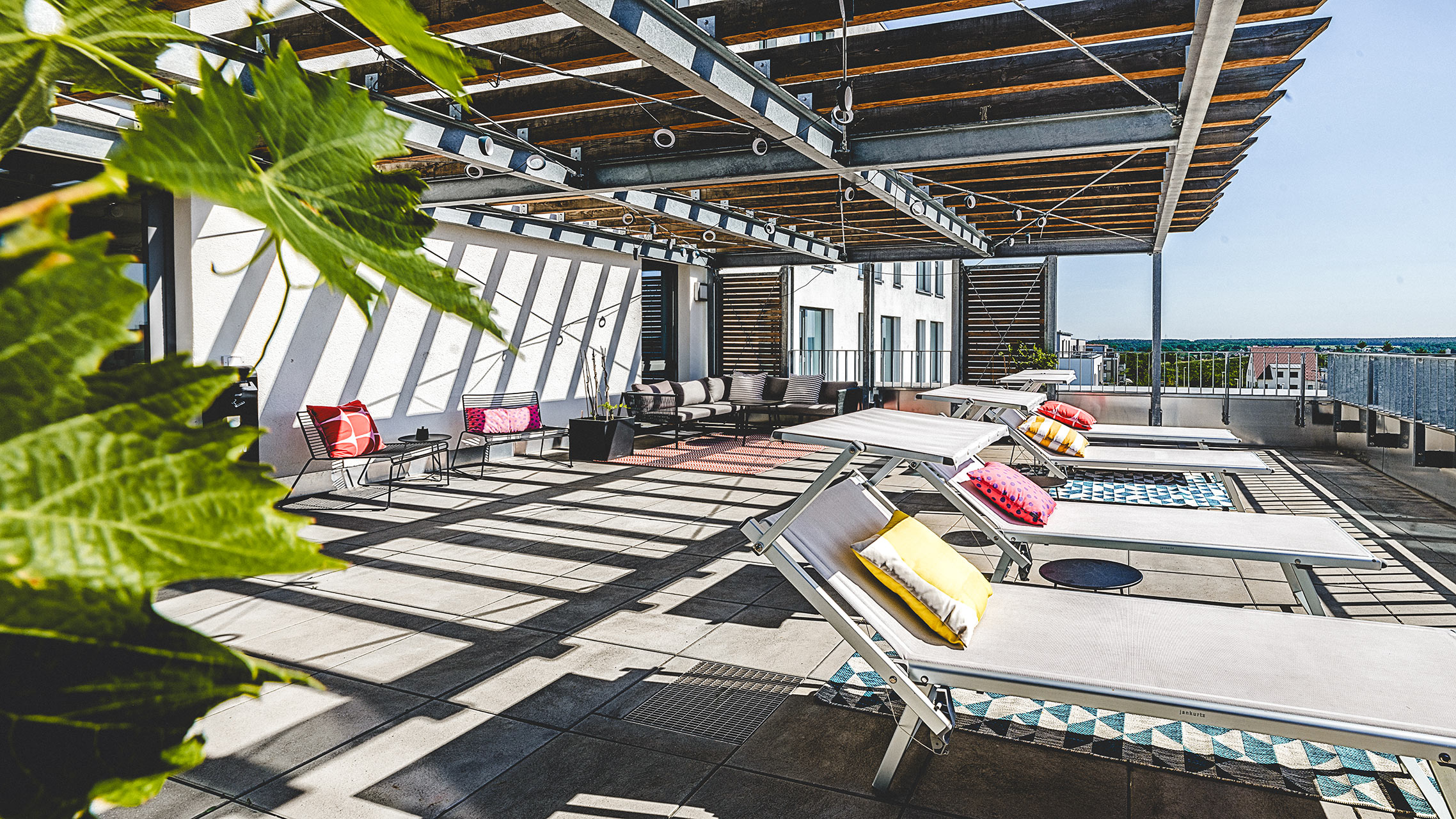 Dachterrasse mit Liegestühlen, bunten Kissen und überdachender Pergola-Konstruktion
