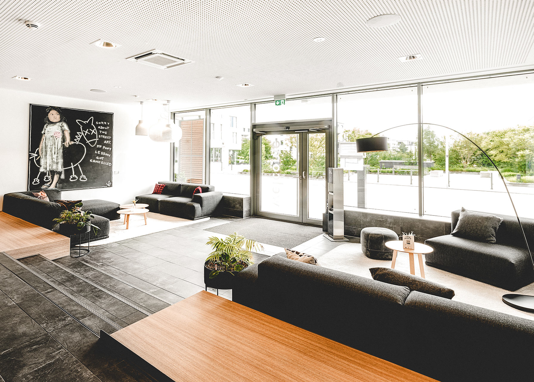 Lobby mit Glaseingangstür, großen Fensterfronten und dunklen Sofalandschaften