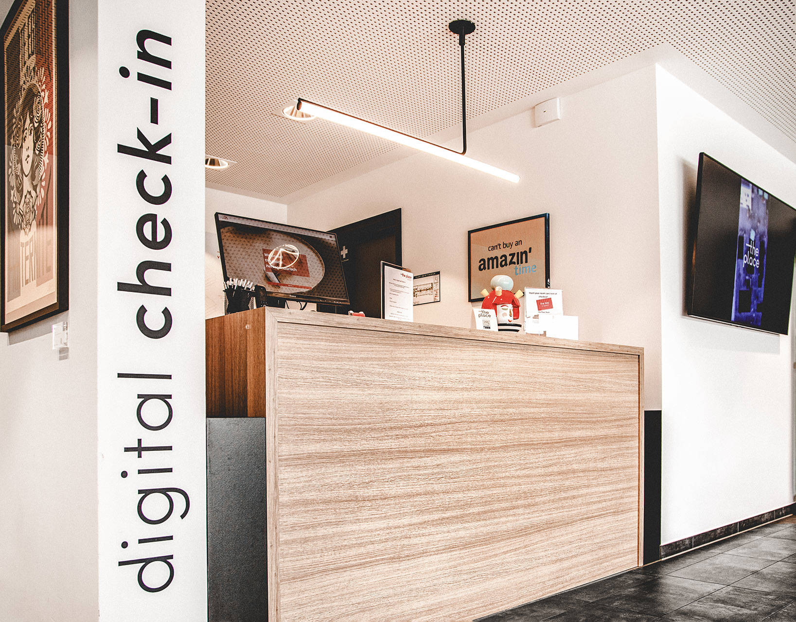 Digitaler Check-in-Bereich mit Holztresen, Bildschirm für Selbst-Check-in und großer Wandschrift