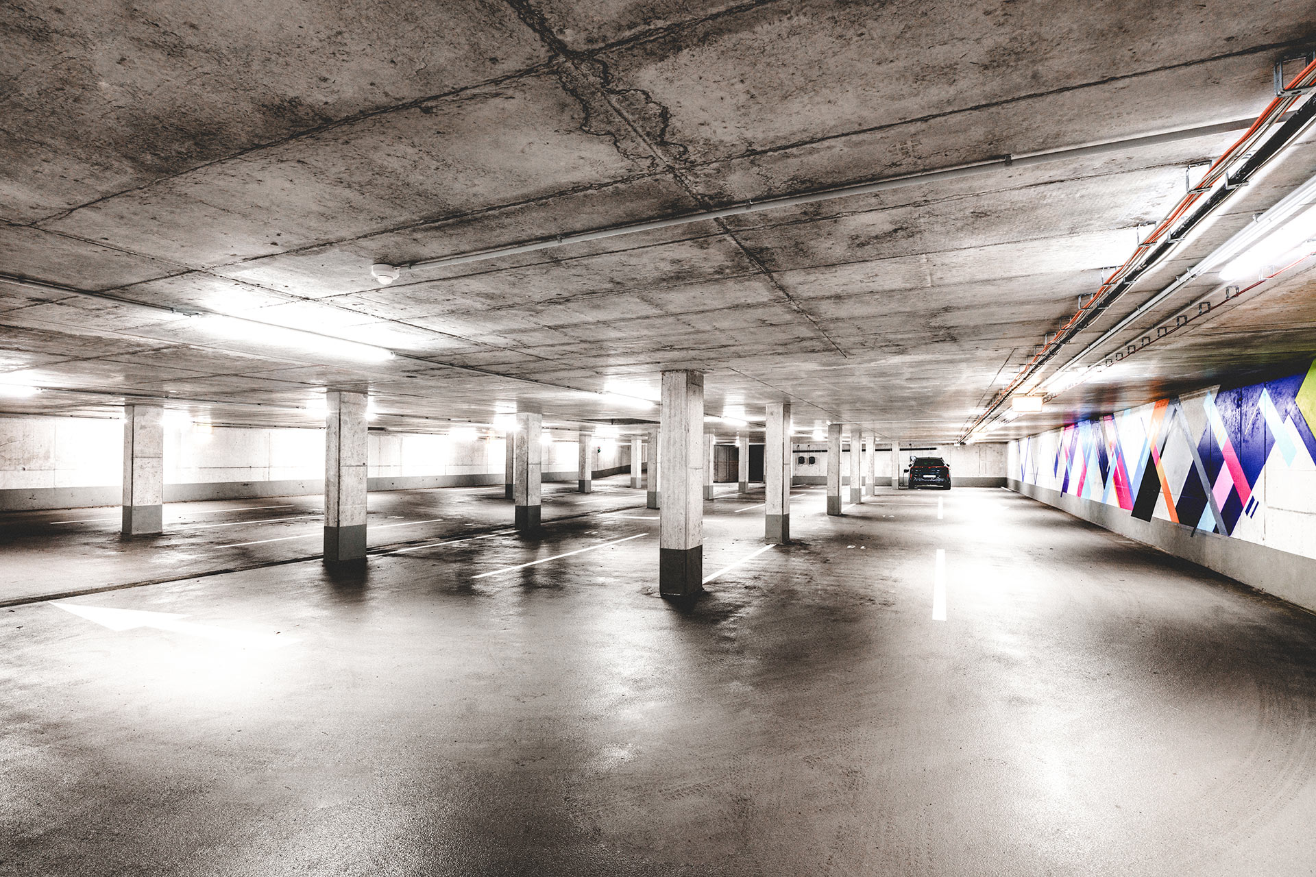 Großzügige Tiefgarage mit Betonstützen, freien Parkplätzen und buntem Wandgemälde